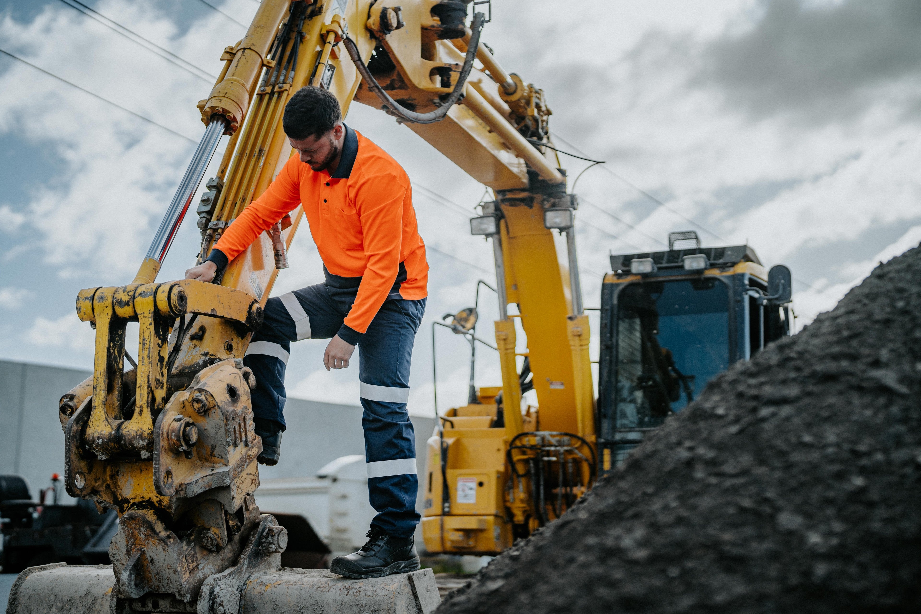 Hard Yakka hi-vis worker stepping off an excavator on a construction site